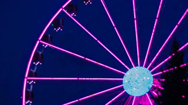 Photo of Pinklight ferris wheel on a dark blue background and with a tree in the front of