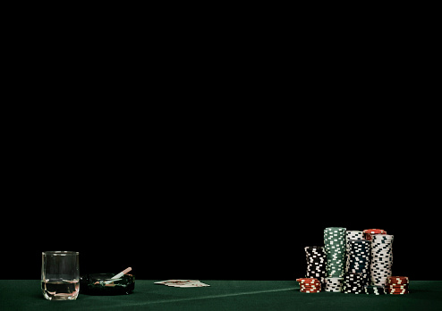 Poker cards with poker chips, hard liquor and ashtray on the table with lot of copy space on black background.
