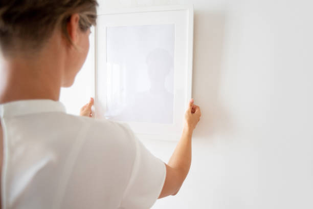 Woman hanging picture frame Woman holding picture frame, hanging it on the white wall adjusting photos stock pictures, royalty-free photos & images