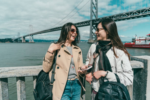 sisters looking each other and laughing two pretty sisters looking each other and laughing joyfully by a background of bridge and ocean. northern california photos stock pictures, royalty-free photos & images