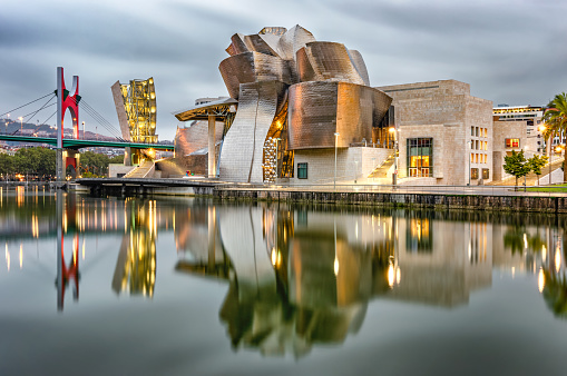 Bilbao, Spain - September 13, 2018: Reflection of the Guggenheim Bilbao museum and La Salve bridge on the Nervion river in Bilbao. The museum was designed by Frank Gehry