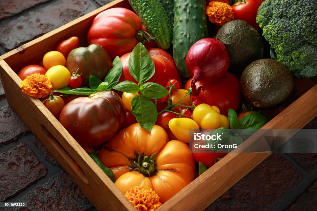 Organic Vegetable box with large, cherry tomatoes, basil, cucumbers, red onions, broccoli and avocado. Organic Vegetable box with large, cherry tomatoes, basil, cucumbers, red onions, broccoli and avocado Agriculture Stock Photo