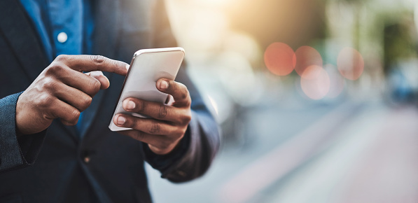 Closeup shot of an unrecognizable businessman using a cellphone in the city