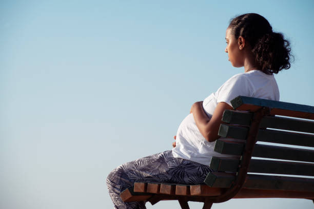 расслабленная беременная женщина сидит на деревянной скамейке. - women sadness african ethnicity african descent стоковые фото и изображения
