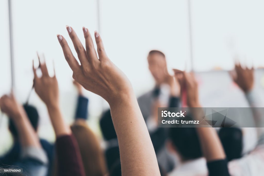 Audience raising hands up while businessman is speaking in training at the office. Education Training Class Stock Photo