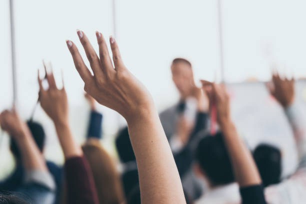 аудитория поднимает руки вверх в то время как бизнесмен говорит в обучении в офисе. - training seminar discussion business стоковые фото и изображения