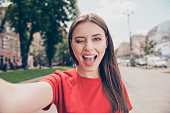 Young woman with dark hair winks and wide open her mouth shooting selfie on the front camera of the smartphone