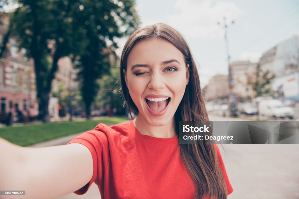 Young woman with dark hair winks and wide open her mouth shooting selfie on the front camera of the smartphone Selfie Stock Photo