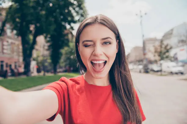 Photo of Young woman with dark hair winks and wide open her mouth shooting selfie on the front camera of the smartphone