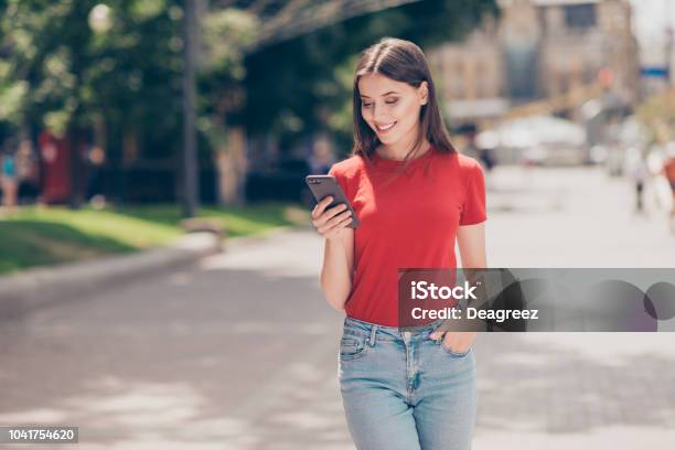 Fit Girl Smiling And Looking Into The Phone Holding Her Hand In The Pocket Of Blue Jeans On A Hot Summer Day Stock Photo - Download Image Now