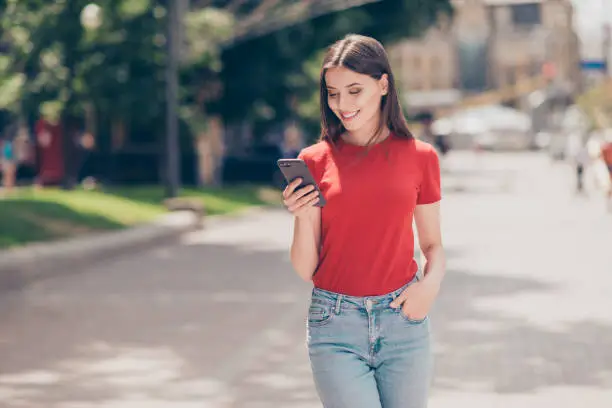 Photo of Fit girl smiling and looking into the phone holding her hand in the pocket of blue jeans on a hot summer day