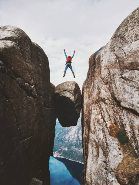 man jumping over kjeragbolten travel in norway kjerag mountains extreme vacations adventure tourist happy emotions success concept - kjeragbolten imagens e fotografias de stock