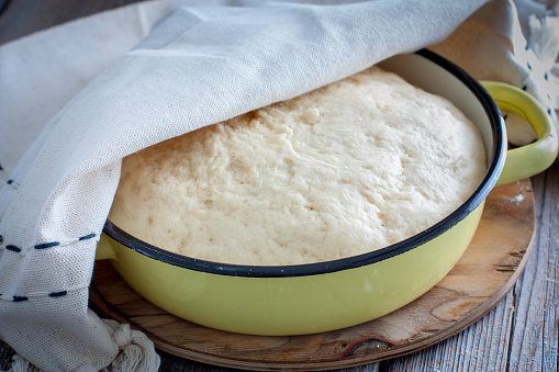 Yeast dough raw in a bowl on a wooden table. Country style, selective focus