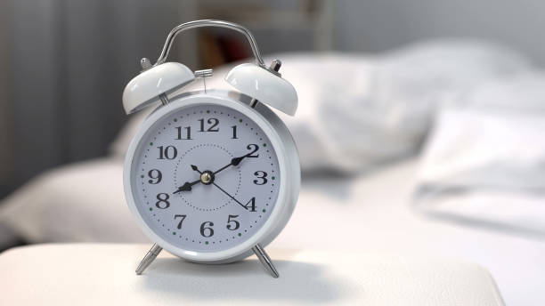 istock Alarm clock showing morning time on night table near bed, sleeping hours 1041785256