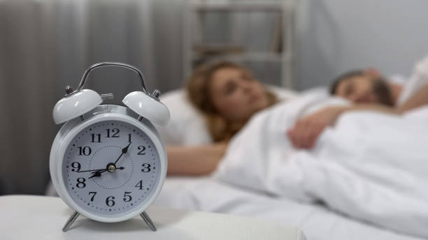 istock Young couple sleeping in bed with ringing alarm clock on table, sleep biorhythms 1041785556