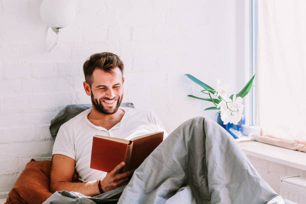 istock Young man reading a book in the bed 1041809952