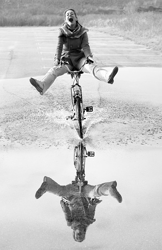 Ecstatic screaming mid adult woman cycling through puddle with reflection. Black and white development (RGB-File).