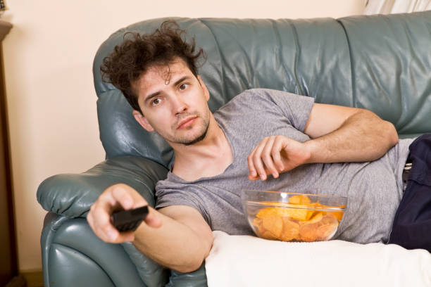 lazy man with the remote and chips on the couch - routine foods and drinks clothing household equipment imagens e fotografias de stock