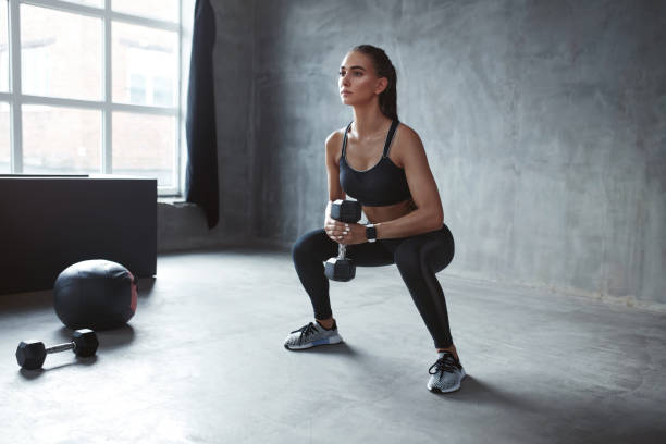 トレーニング。スクワットを行うファッション スポーツウェア スポーツ女性 - crouching ストックフォトと画像