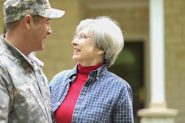 Family welcomes home USA army soldier. Family welcomes home a USA army soldier. Mother excitedly hugs adult son, who wears combat uniform and carries duffle bag. They stand in front of mother's home. proud army mom stock pictures, royalty-free photos & images