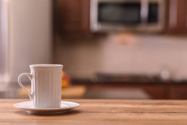 istock Defocused kitchen with coffee cup on empty wooden table foreground. 1041853944