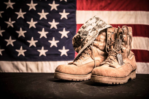 American Veteran's Day theme with military boots, hat, USA flag. USA military boots, hat and dog tags with American flag in background. No people in this US Memorial Day or Veteran's Day image. usa flag shoes stock pictures, royalty-free photos & images
