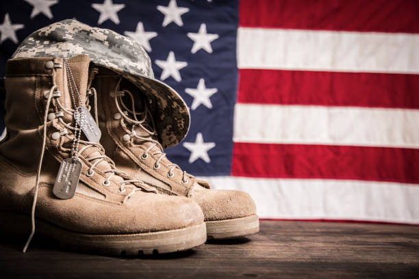 USA military boots, hat and dog tags with American flag in background.  No people in this US Memorial Day or Veteran's Day image.