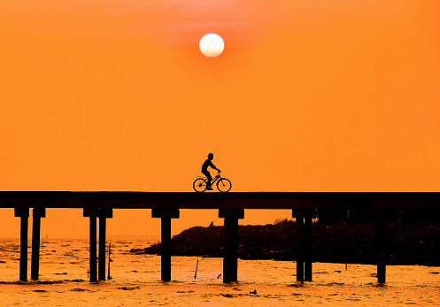 Silhouette, People are cycling on a wooden bridge. Under the sun is going down.