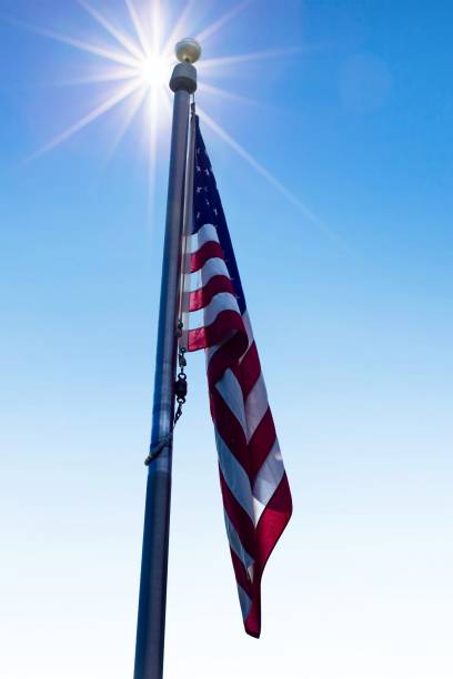 Bright sunbeam shining over a United States Flag on a pole against the blue sky