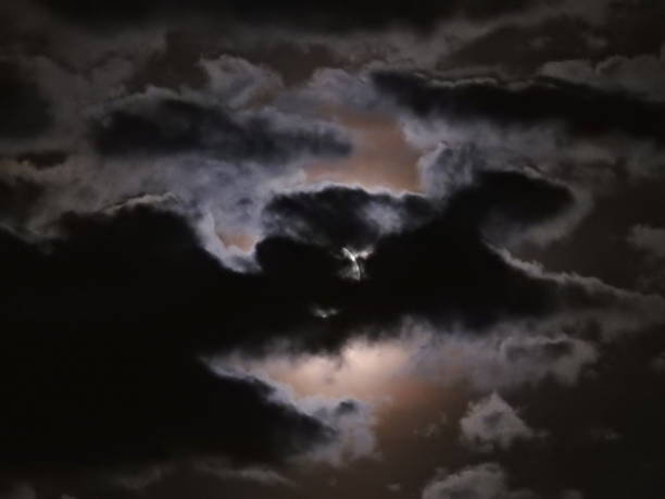 The wide angle of full moon hidden behind clouds at dusk sky.