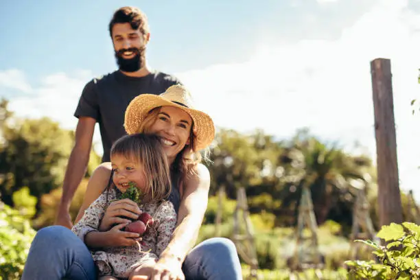 Young man gives his woman and daughter ride in wheelbarrow. Happy family a ride in wheelbarrow at farm.