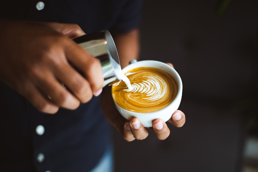 Barista making a cup of coffee latte art in coffee shop.