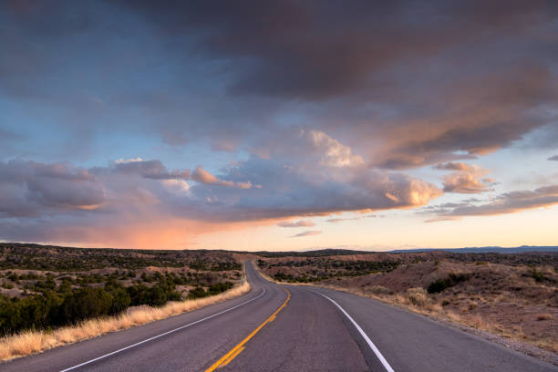 пустынное шоссе, изгибаемое в драматический закат под красивыми облаками - desert road desert road landscape стоковые фото и изображения
