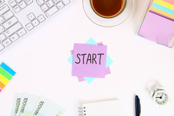 istock Text Start on the sticker note on the white desktop next to the coffee mug and the keyboard. Top view, flat layout. 1041939226