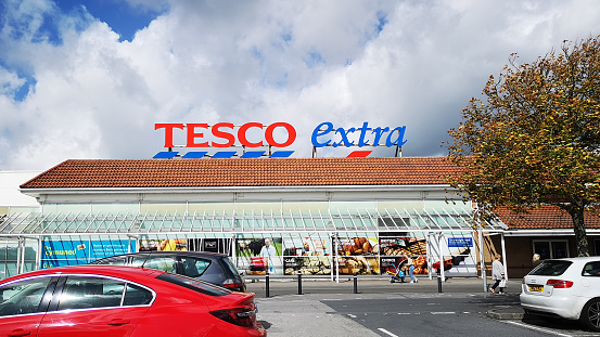Llanelli, UK: September 21, 2018: Customers park their cars and enter a Tesco Extra superstore. Tesco is a British multinational groceries and general merchandise retailer. It is the third-largest retailer in the world measured by gross revenues.