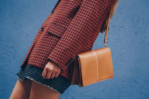 Photo of attractive woman wearing a  mini skirt, check plaid blazer and a lether brown tote bag. fashion outfit perfect for autumn. style of 2018 autumn.