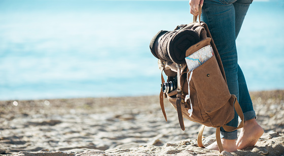 Woman traveler stand on the sand beach and holding backpack. Concept of travel.