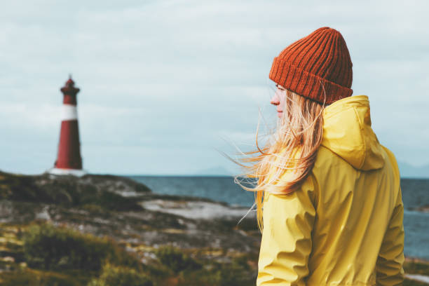 mujer consejos faro mar paisaje noruega viajes vida concepto escandinavo unas vacaciones al aire libre. pelo de la chica rubia en viento llevando sombrero naranja y amarillo impermeable - cultura escandinava fotografías e imágenes de stock