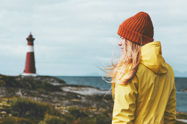 노르웨이 여행 라이프 스타일 개념 스칸디나비아 휴가 야외에서 여자 관광 등 대 바다 풍경. 주황색 모자와 노란 우비를 입고 바람에 금발 여자 머리 - 북유럽 뉴스 사진 이미지