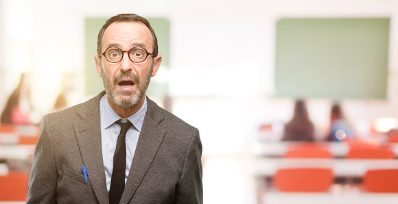 Teacher man using glasses scared in shock, expressing panic and fear at classroom