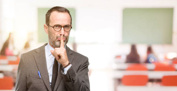 istock Teacher man using glasses with index finger on lips, ask to be quiet. Silence and secret concept 1041972748