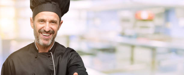 istock Senior cook man, wearing chef hat holds hands welcoming in handshake pose, expressing trust and success concept, greeting 1041973192