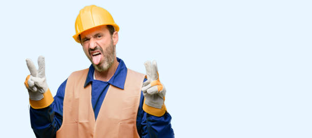 istock Senior engineer man, construction worker looking at camera showing tong and making victory sign with fingers 1041977810