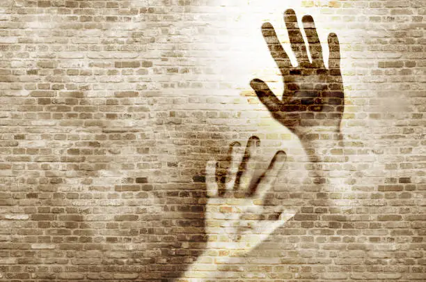 Graffiti/shadow on a brickwall showing human hands up against the wall