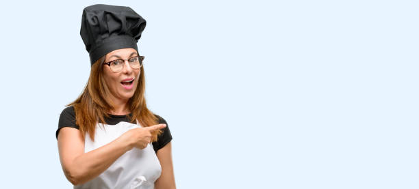 istock Middle age cook woman wearing chef apron pointing away side with finger 1042007642