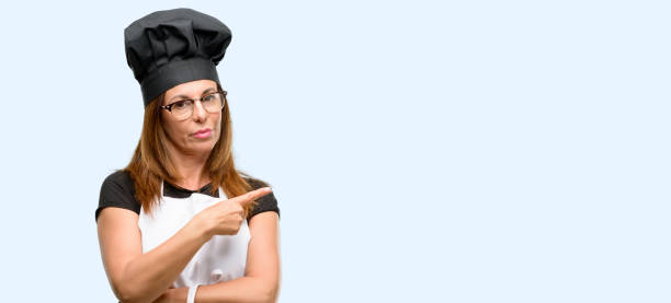 istock Middle age cook woman wearing chef apron pointing away side with finger 1042008018