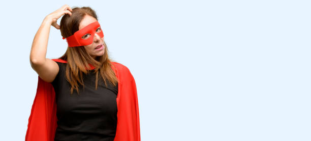 Middle age super hero woman wearing red mask and cape doubt expression, confuse and wonder concept, uncertain future