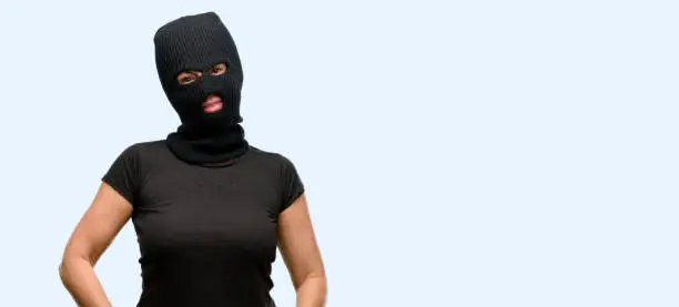 Burglar terrorist woman wearing balaclava ski mask confident and happy with a big natural smile laughing isolated blue background