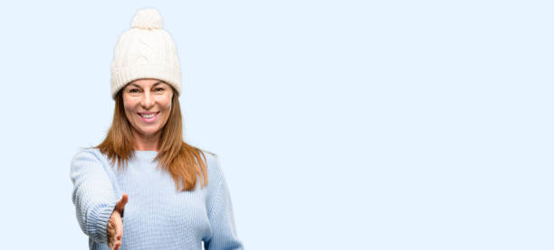 istock Middle age woman wearing wool winter cap holds hands welcoming in handshake pose, expressing trust and success concept, greeting 1042012372