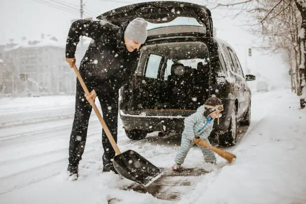 Photo of Father and little son cleaning snow around car